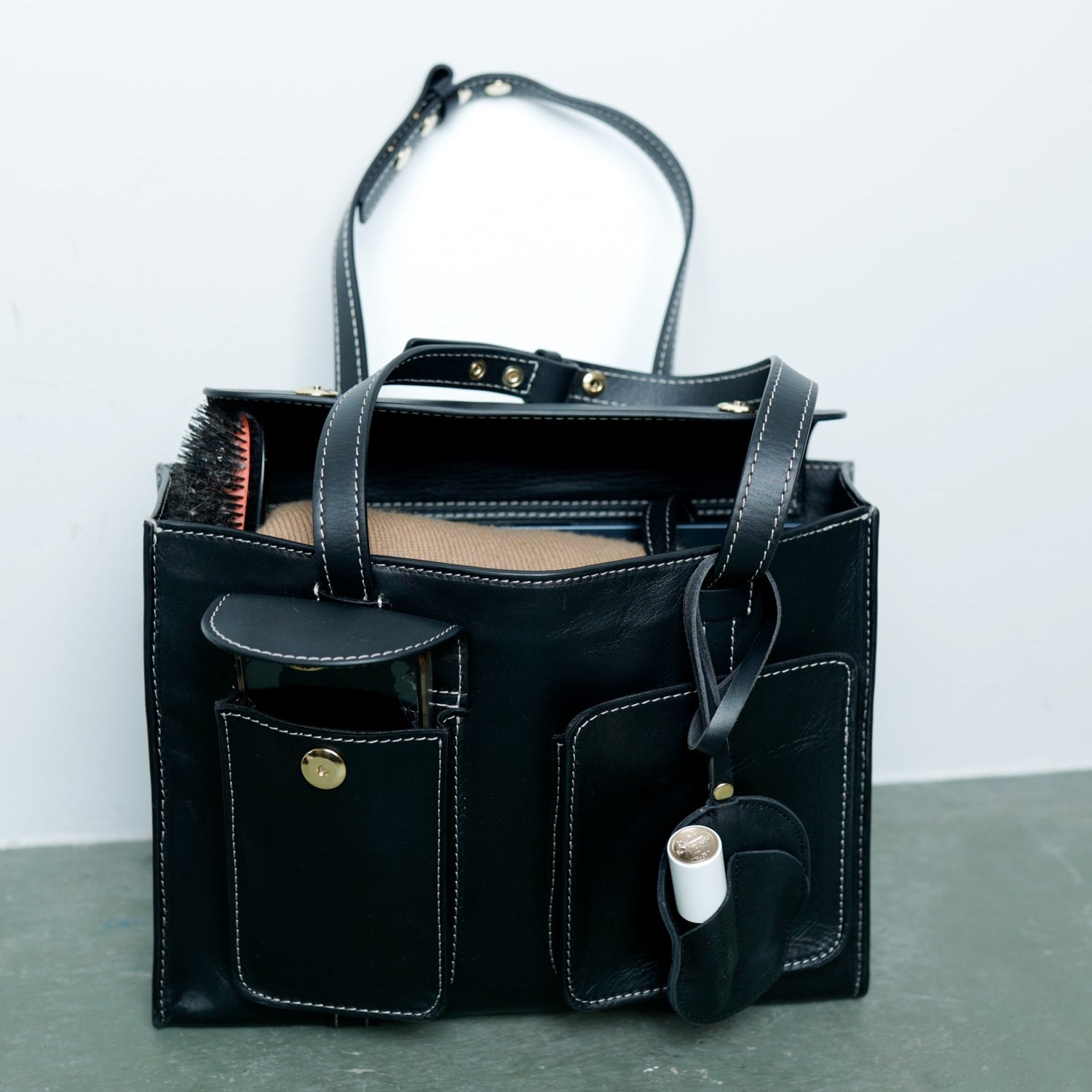 Black leather tote bag with various items on a gray surface and light gray background