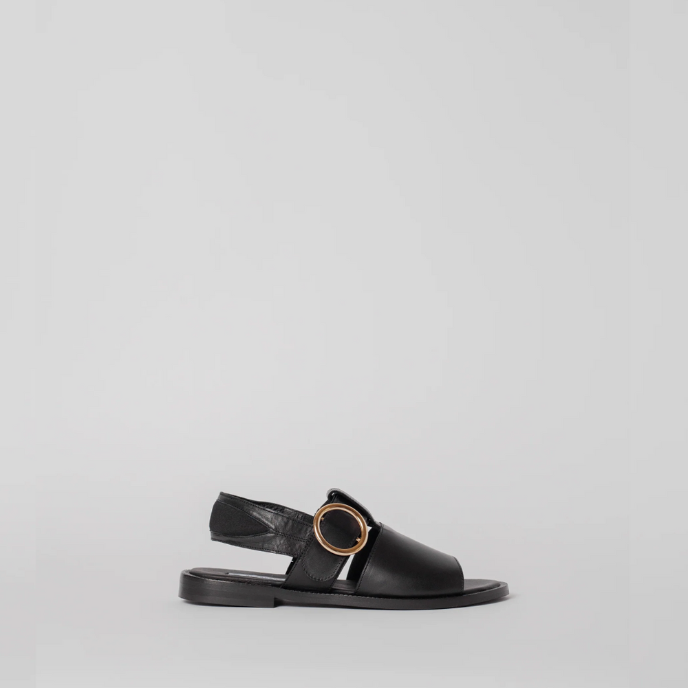 Black sandal with a gold ring on a light gray background